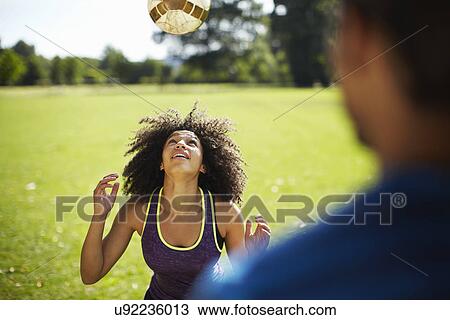 Stock Image - Young woman heading football in park. Fotosearch