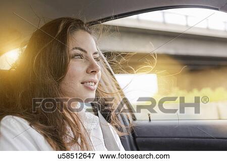 Stock Photo - Young woman in car, hair blowing in wind. Fotosearch