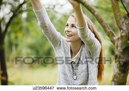 Young woman in field holding on to tree branch View Large Photo Image Stock Photo - Young woman in field holding on to tree branch. Fotosearch