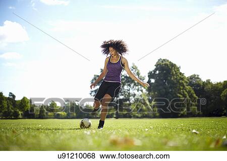 Stock Photo - Young woman kicking soccer ball in park. Fotosearch