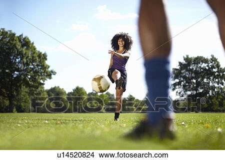 Picture - Young woman kicking soccer ball toward boyfriend in park. Fotosearch