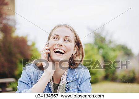 Young woman laughing whilst chatting on smartphone in park View Large Photo Image Stock Photo - Young woman laughing whilst chatting on smartphone in park. Fotosearch