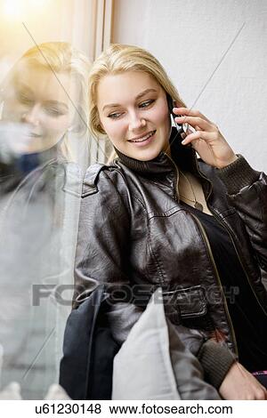 Stock Photo - Young woman on chatting smartphone whilst looking out of window. Fotosearch
