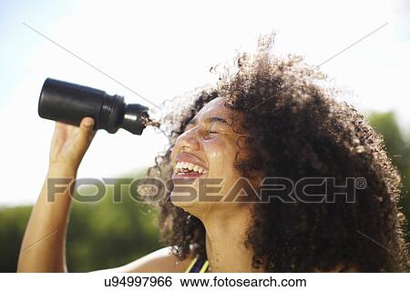 Stock Photograph - Young woman pouring water onto face in park. Fotosearch