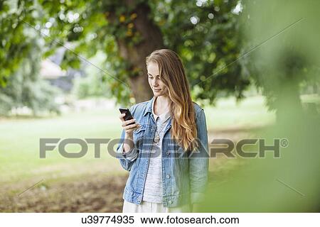 Young woman reading texts on smartphone in park View Large Photo Image Stock Photography - Young woman reading texts on smartphone in park. Fotosearch
