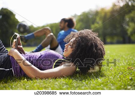 Stock Photography - Young woman taking a break reading texts on smartphone in park. Fotosearch