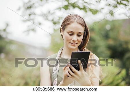 Stock Photograph - Young woman using touchscreen on digital tablet in field. Fotosearch