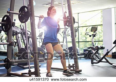 Stock Image - Young woman weight lifting with barbell. Fotosearch
