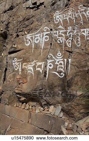 Stock Image - Bhutanese script on rocks with religious figurine, Paro Valley, Paro District, Bhutan. Fotosearch
