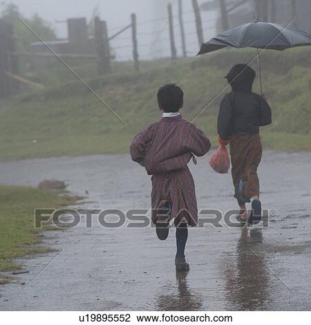Stock Image - Children running in the rain in Laptshaka, Punakha Valley Bhutan. Fotosearch