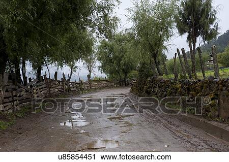 Stock Image - Dirt road passing through mountains, Phobjikha Valley, Bhutan. Fotosearch