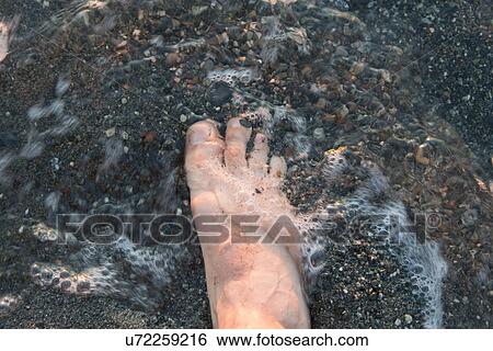Stock Photograph - Human foot in water on the beach, Trout River, Gros Morne National Park, Newfoundland and Labrador, Canada. Fotosearch