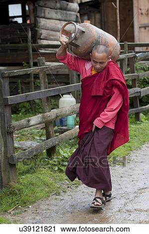 Stock Image - Monk carrying a cylinder Gangte Goemba in the background, Phobjikha Valley, Bhutan. Fotosearch