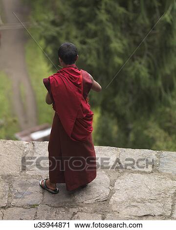Stock Image - Monk standing on a stone wall at Tango Goemba, Thimphu, Bhutan. Fotosearch