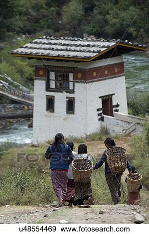 Stock Photo - Women carrying baskets with Tamchhog Lhakhang in the background, Paro Valley, Paro District, Bhutan. Fotosearch