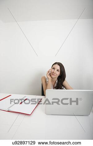 Beautiful businesswoman looking away while answering cell phone at desk in office View Large Photo Image Stock Photo - Beautiful businesswoman looking away while answering cell phone at desk in office. Fotosearch