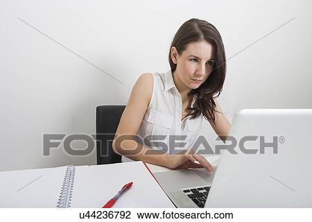 Stock Image - Beautiful businesswoman using laptop at desk in office. Fotosearch