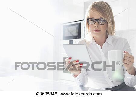 Beautiful mid adult businesswoman having coffee while using table PC at home View Large Photo Image Stock Photography - Beautiful mid adult businesswoman having coffee while using table PC at home. Fotosearch