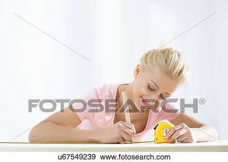 Stock Photo - Beautiful woman marking table with measure tape. Fotosearch