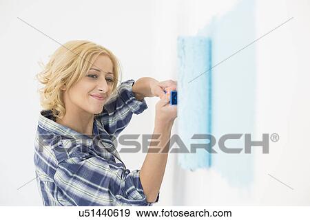 Stock Photo - Beautiful woman painting wall with paint roller. Fotosearch