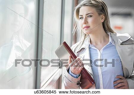 Stock Photography - Beautiful young businesswoman looking through glass at railroad station. Fotosearch