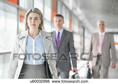 Stock Photo - Beautiful young businesswoman walking with male colleagues in background at train platform. Fotosearch
