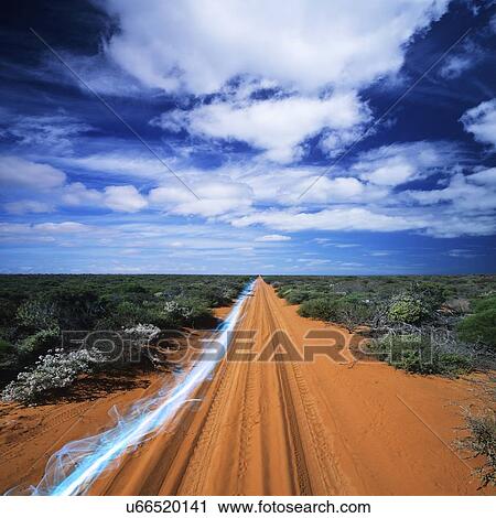 Stock Image - Blue streak of light on dirt road against cloudy sky. Fotosearch