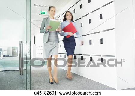 Stock Image - Blurred view of businesswomen walking in office. Fotosearch