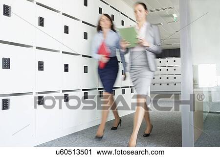 Stock Image - Blurred view of businesswomen walking in office. Fotosearch