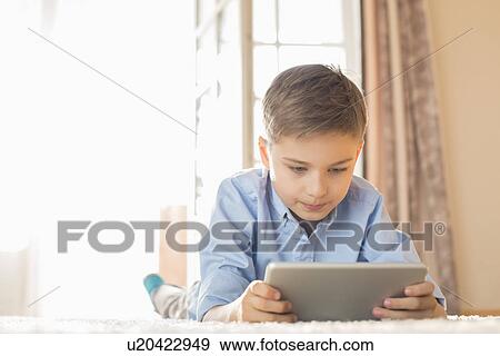 Stock Photo - Boy using digital tablet while lying on floor at home. Fotosearch