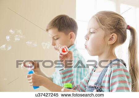 Stock Photography - Brother and sister playing with bubble wands at home. Fotosearch