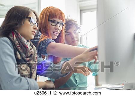 Stock Image - Business colleagues discussing over computer in creative office. Fotosearch