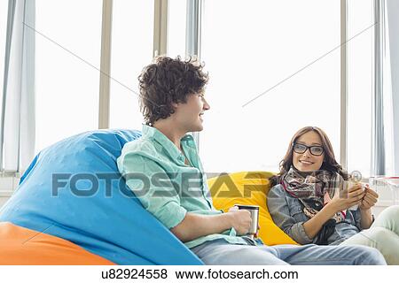 Stock Photo - Business colleagues having coffee while relaxing on beanbag chairs in creative office. Fotosearch