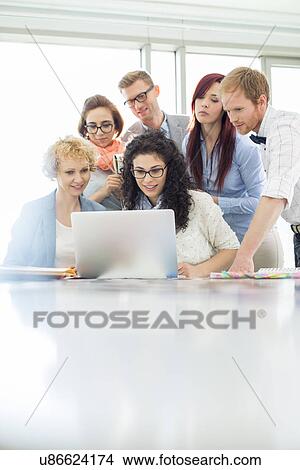 Business colleagues using laptop at desk in creative office View Large Photo Image Picture - Business colleagues using laptop at desk in creative office. Fotosearch