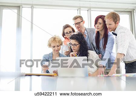 Stock Image - Business colleagues with laptop analyzing document in creative office. Fotosearch