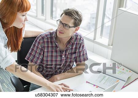 Business couple looking at each other while using laptop in creative office View Large Photo Image Stock Photo - Business couple looking at each other while using laptop in creative office. Fotosearch