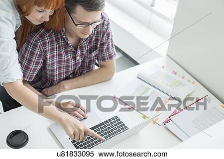 Stock Photography - Business couple using laptop in creative office. Fotosearch