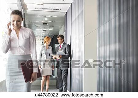 Business people discussing in corridor with colleague using cell phone in foreground View Large Photo Image Stock Image - Business people discussing in corridor with colleague using cell phone in foreground. Fotosearch