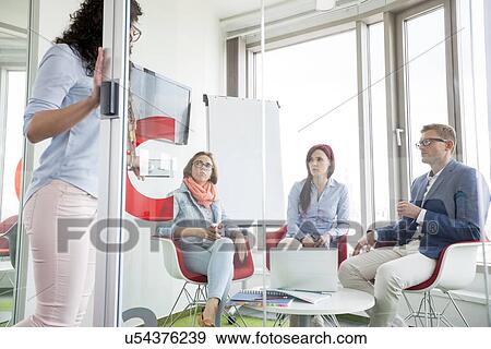 Business people looking at female colleague standing in sliding door View Large Photo Image Stock Photo - Business people looking at female colleague standing in sliding door. Fotosearch