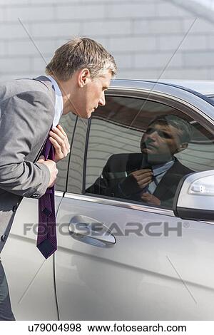 Businessman adjusting tie while looking in car window View Large Photo Image Stock Photo - Businessman adjusting tie while looking in car window. Fotosearch