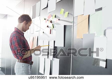 Businessman analyzing documents on wall at creative office View Large Photo Image Stock Image - Businessman analyzing documents on wall at creative office. Fotosearch