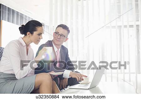 Picture - Businessman and businesswoman discussing over laptop in office. Fotosearch
