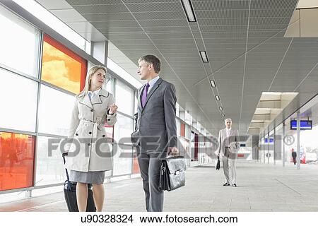 Businessman and businesswoman conversing while walking in railroad station View Large Photo Image Picture - Businessman and businesswoman conversing while walking in railroad station. Fotosearch
