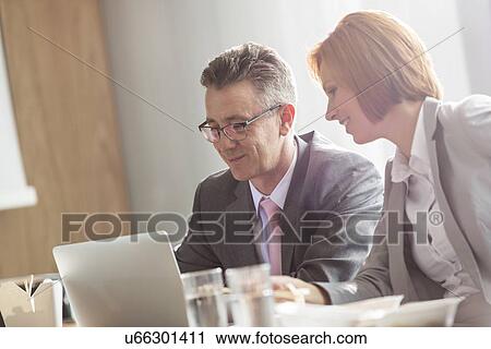 Stock Image - Businessman and businesswoman discussing while having lunch in office. Fotosearch