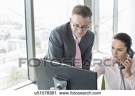 Stock Image - Businessman and businesswoman working together in office. Fotosearch