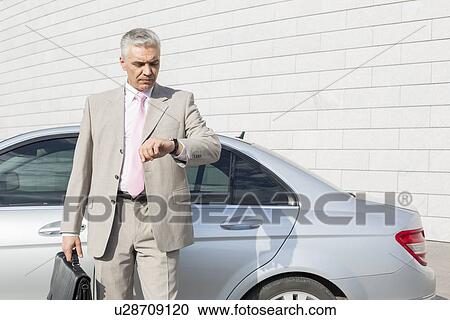Businessman checking the time in front of car outdoors View Large Photo Image Stock Image - Businessman checking the time in front of car outdoors. Fotosearch