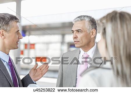 Stock Image - Businessman communicating with colleagues on railroad platform. Fotosearch