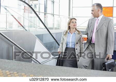 Businessman conversing with female colleague while walking up stairs in train station View Large Photo Image Stock Image - Businessman conversing with female colleague while walking up stairs in train station. Fotosearch
