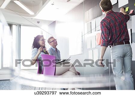Stock Photo - Businessman explaining documents to colleagues in creative office. Fotosearch