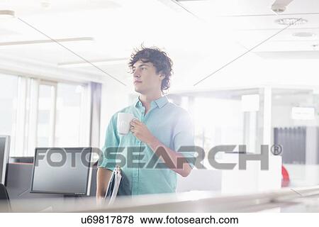 Businessman having coffee while holding files in creative office View Large Photo Image Stock Photo - Businessman having coffee while holding files in creative office. Fotosearch